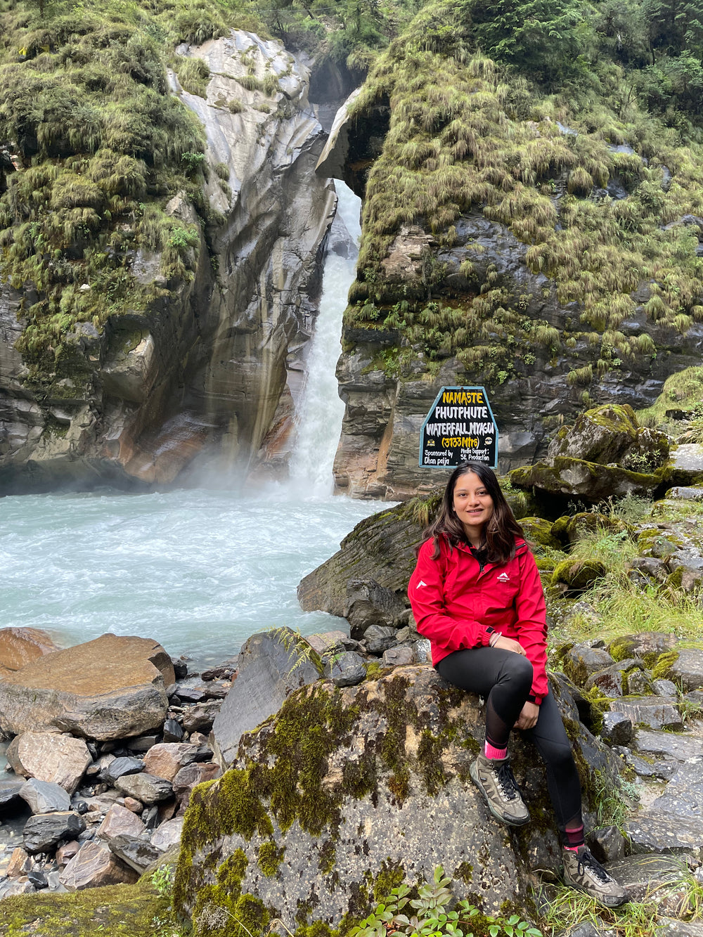 Owner of virohana in a red jacket sitting on a rock by a waterfall