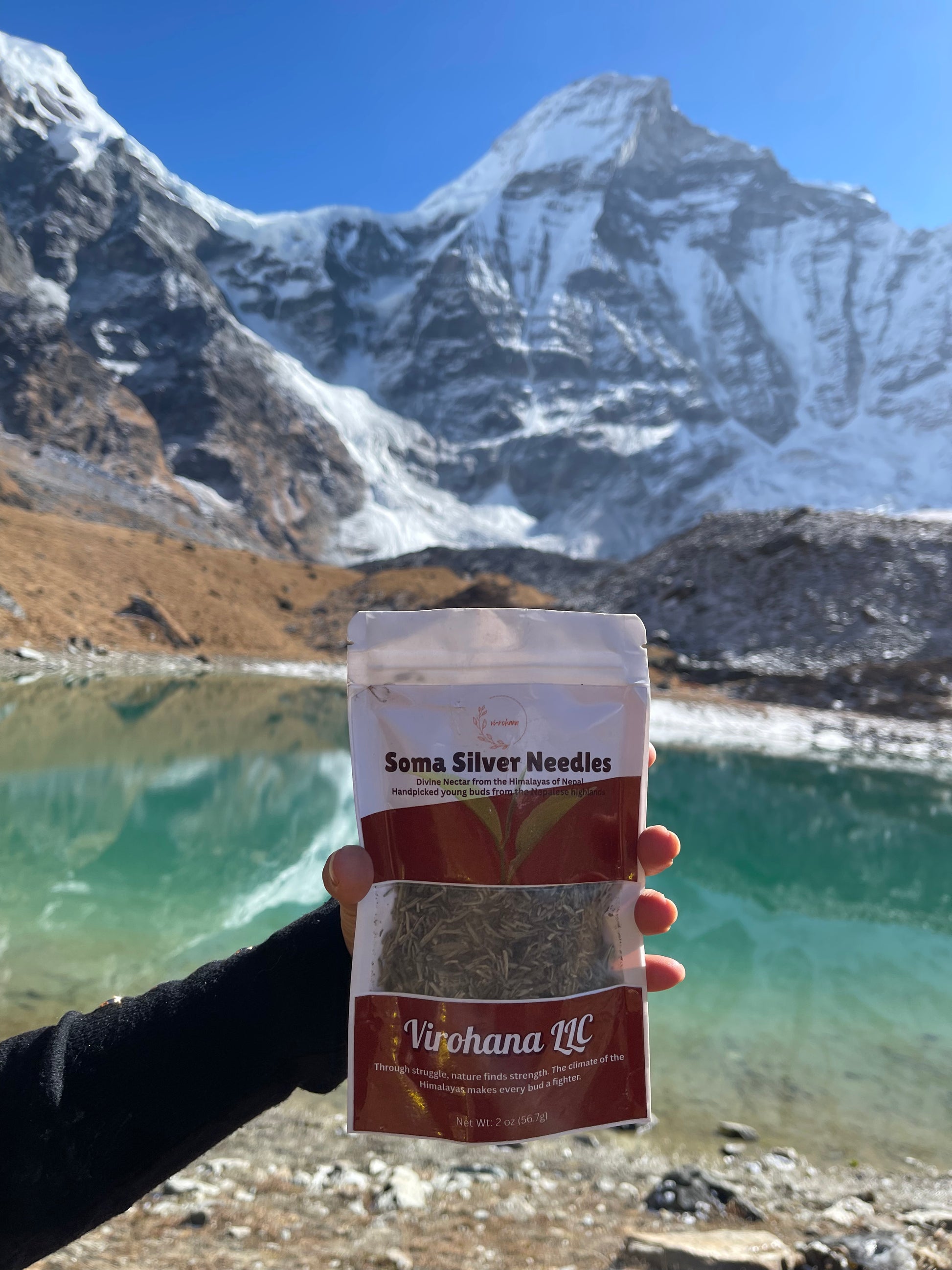 Hand holding a package of Soma Silver Needles in front of a mountain lake