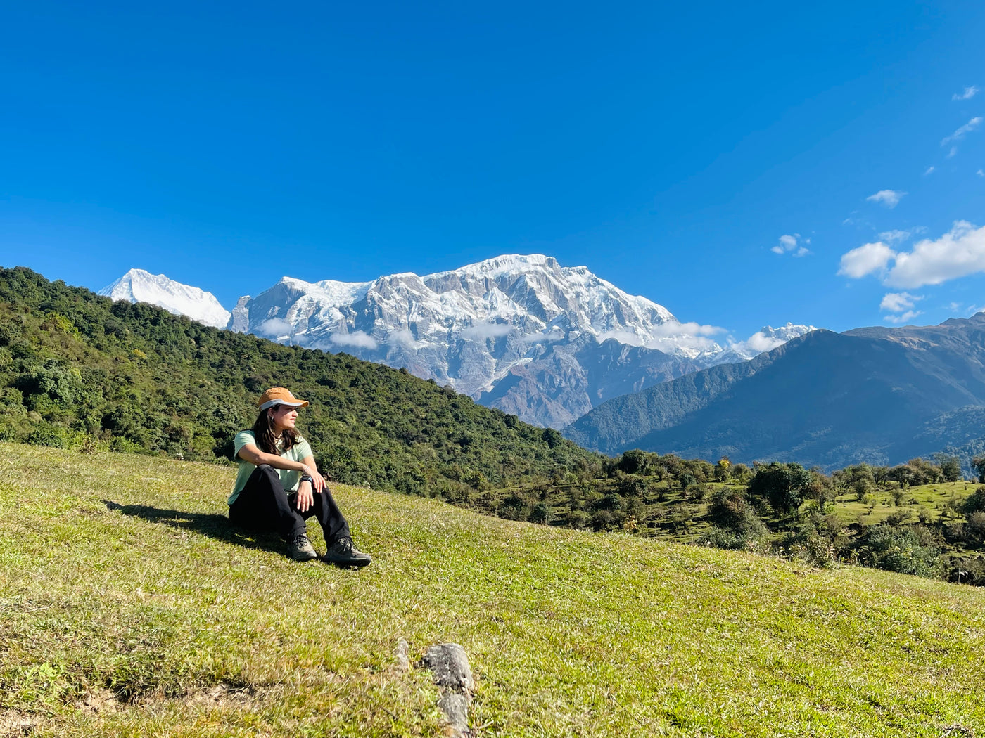 Owner of virohana sitting on a grassy hill with snow-capped mountains in the background