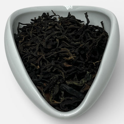 Black tea leaves in a white triangular dish on a white background