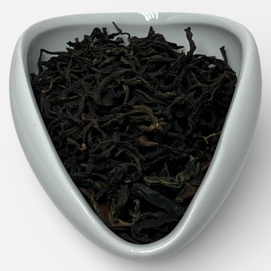 Black tea leaves in a white triangular dish on a white background