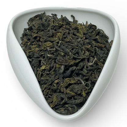 Triangular white dish filled with green tea leaves on a white background