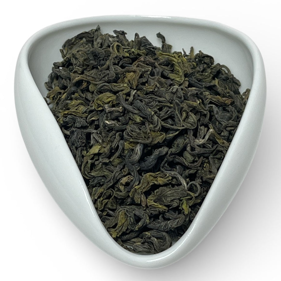 Triangular white dish filled with green tea leaves on a white background
