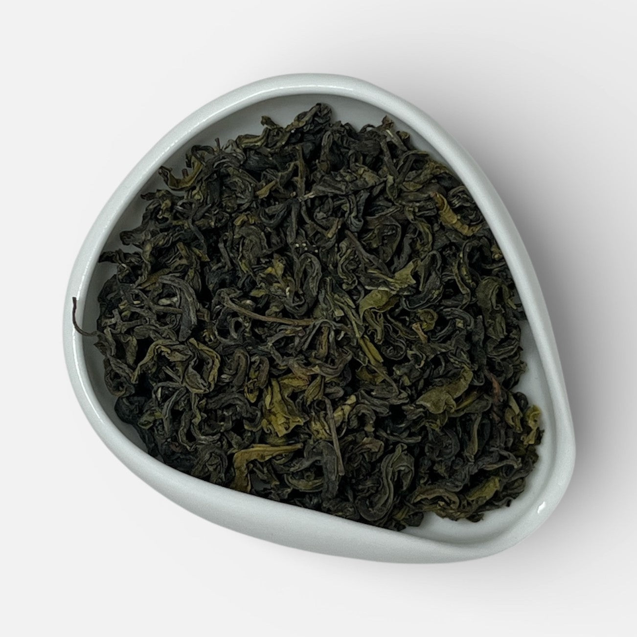 Triangular white dish filled with green tea leaves on a white background