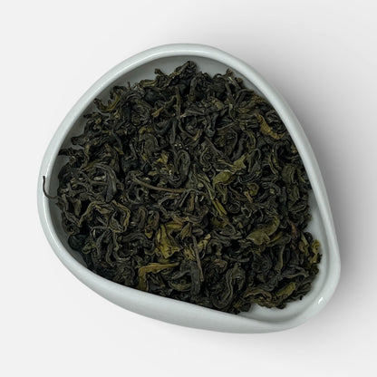 Triangular white dish filled with green tea leaves on a white background
