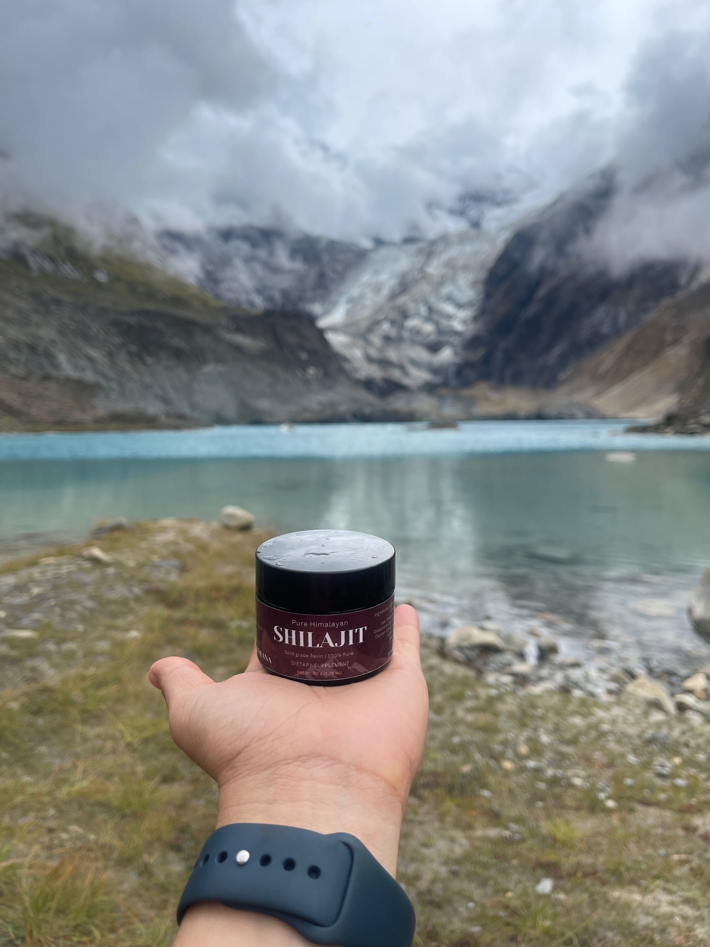 Hand holding a jar labeled 'Shilajit' with a mountainous landscape in the background