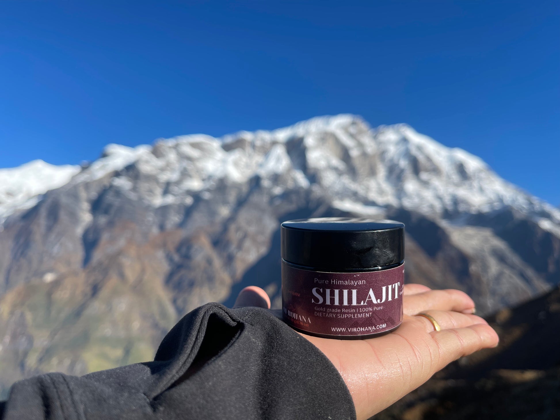 Person holding a Shilajit container with a mountainous landscape in the background