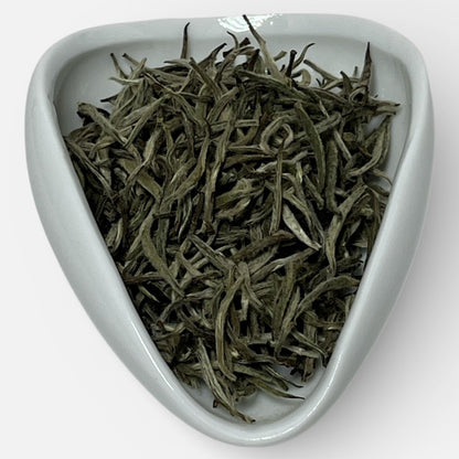 Dry tea leaves in a white triangular ceramic dish on a white background