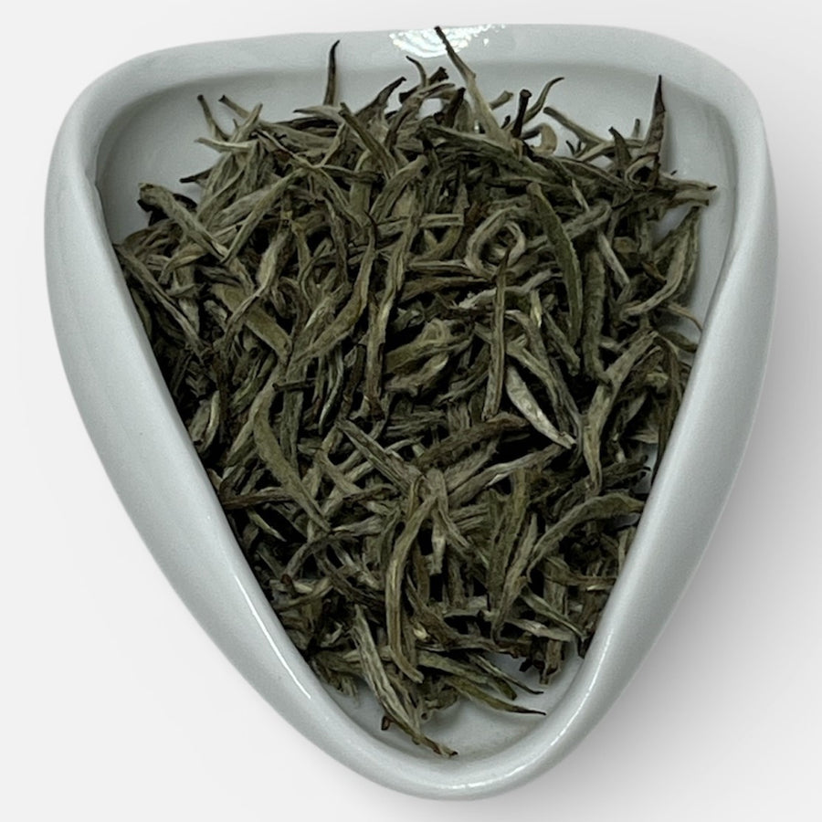 Dry tea leaves in a white triangular ceramic dish on a white background